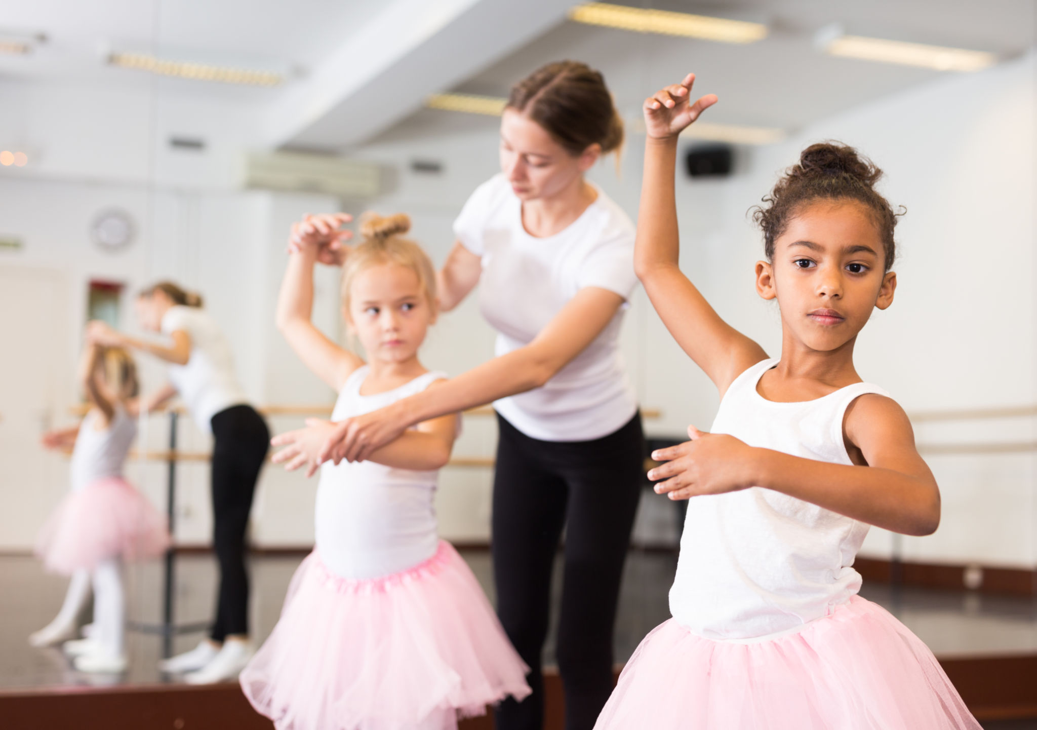 Young ballet students in pink tutus practicing at the barre with their instructor at Woodbridge School of Dance